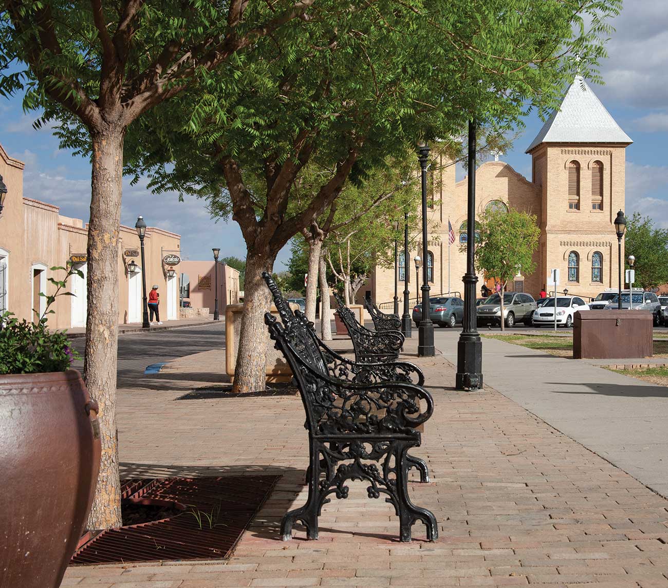 A view of the Mesilla Plaza with a bench, trees, and historic basilica.
