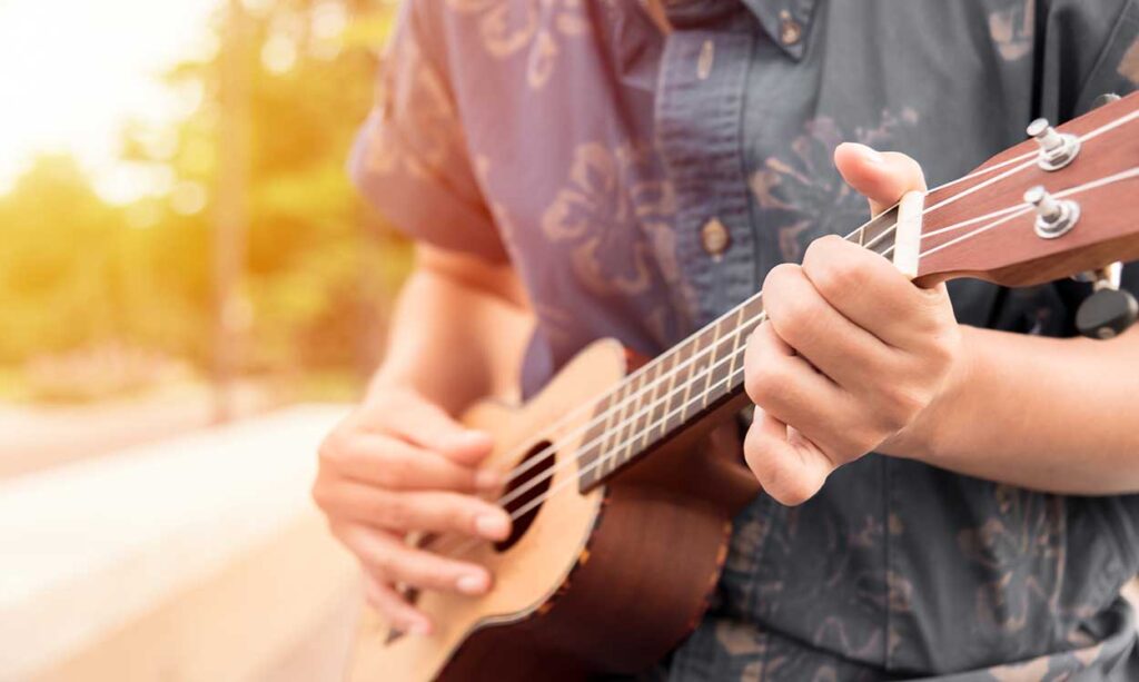 Person playing an ukulele outdoors.