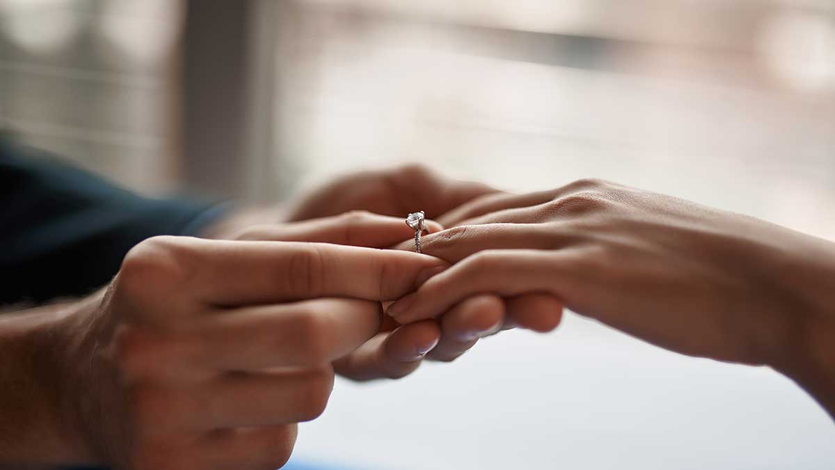 Man placing a diamond engagement ring on a woman's hand.