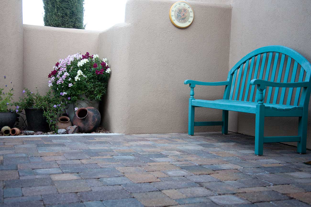 Patio area made with pavers, with bench and potted plants