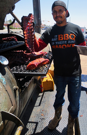 owner of rollin smoke holding a rack of ribs by his smoker