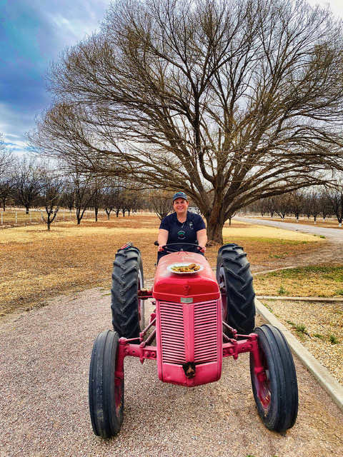Kristen Worthington delivers a pecan-centric gourmet dinner in authenticfarm-to-table style. In this photo from the book "Slow Travel New Mexico," Kristen is driving a red tractor with a plate of food on the front.