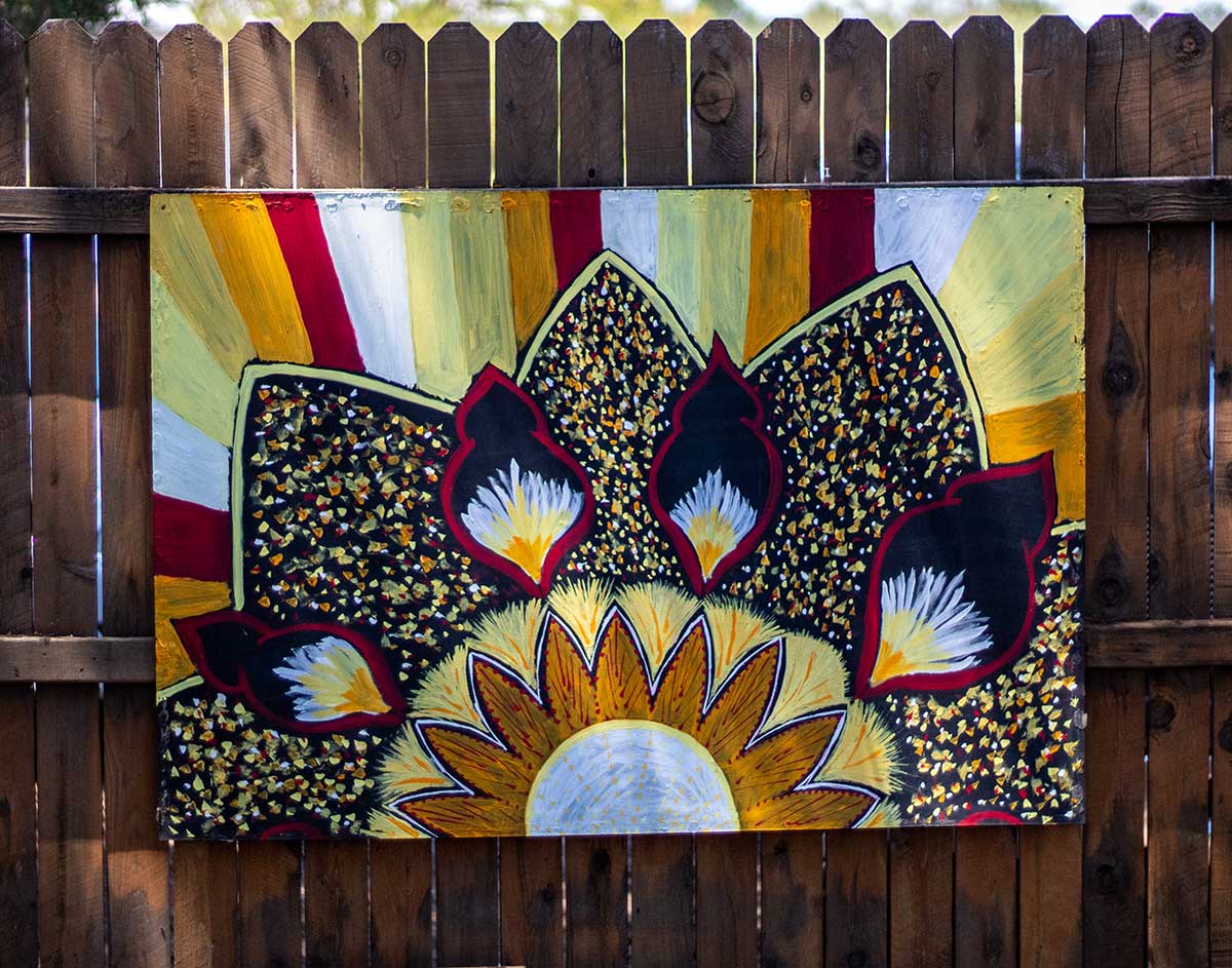 Painted mandala hanging on fence.